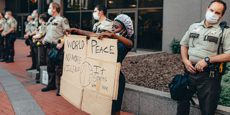 african girl holding a signage board about world peace with several police men at her side